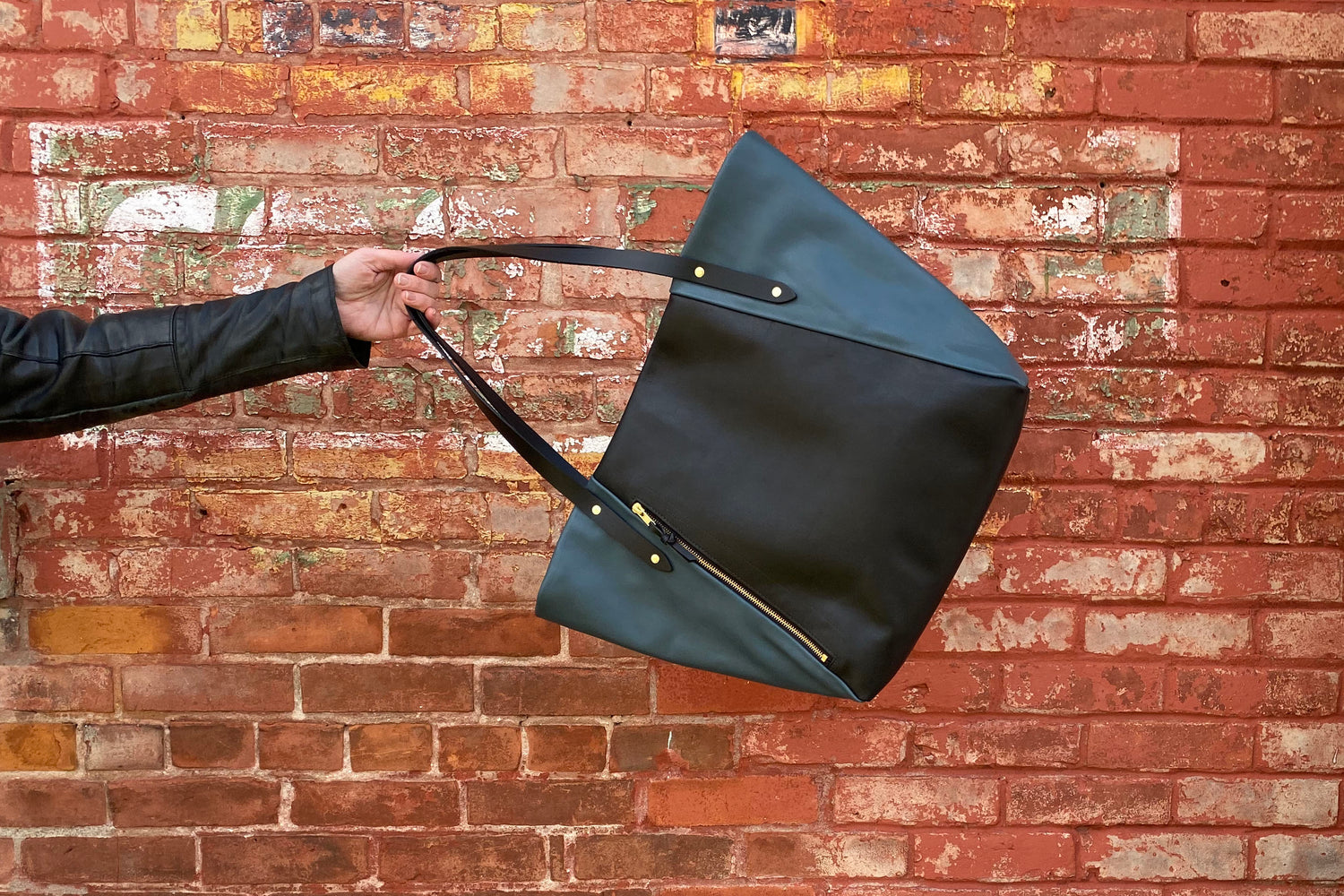 A black and petrol blue bag in front of a red brick wall