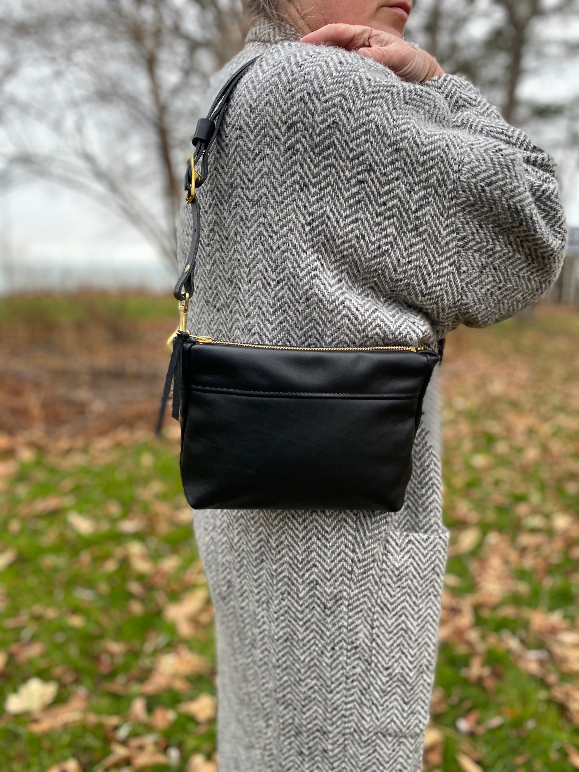 Studio pothos Cosmos bag in black with brass hardware, worn as a purse.