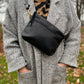 Cosmos bag in midnight black with brass clasps, worn with a short strap over a beige herringbone jacket