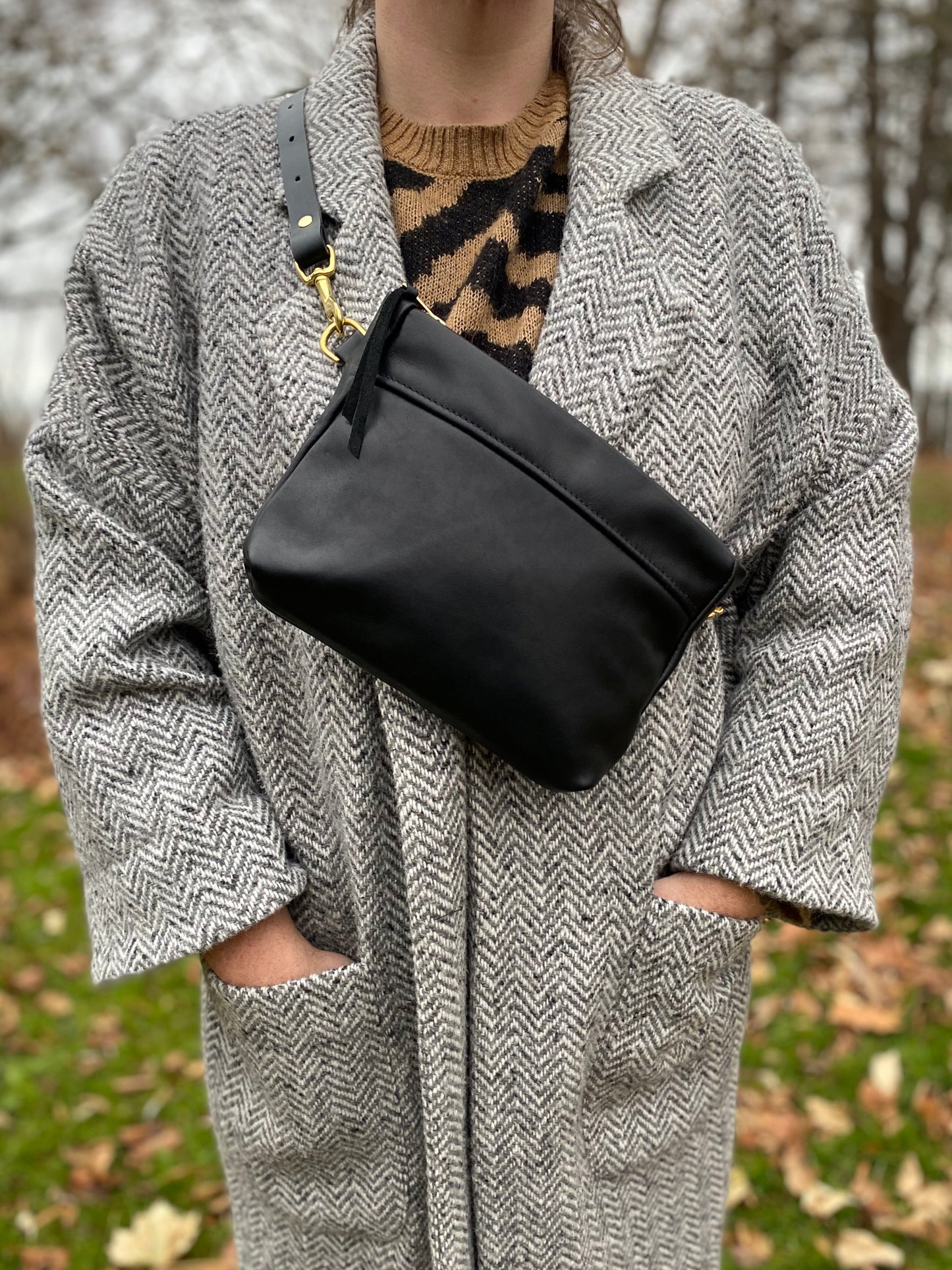 Cosmos bag in midnight black with brass clasps, worn with a short strap over a beige herringbone jacket