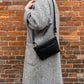 Studio pothos Cosmos bag in black with brass hardware, worn with a long strap.