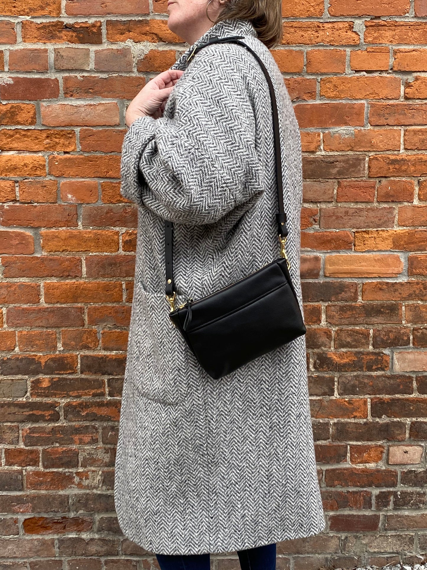 Studio pothos Cosmos bag in black with brass hardware, worn with a long strap.