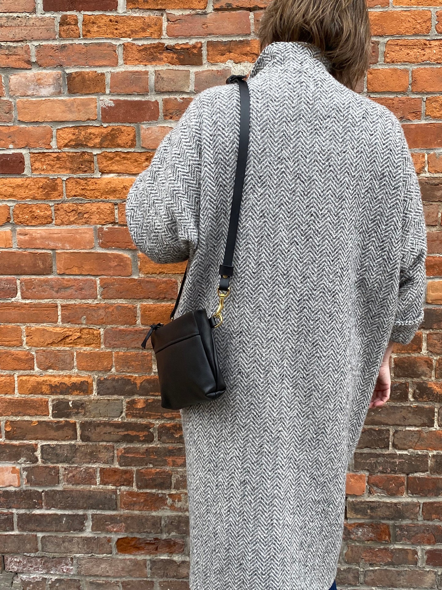 Studio pothos Cosmos bag in black with brass hardware, worn with a long strap.